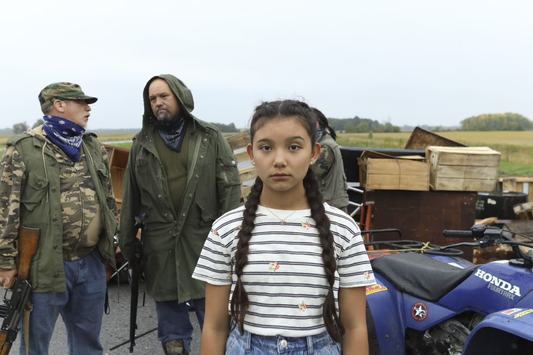 Young girl in a film in front of two men with guns and a honda four runner