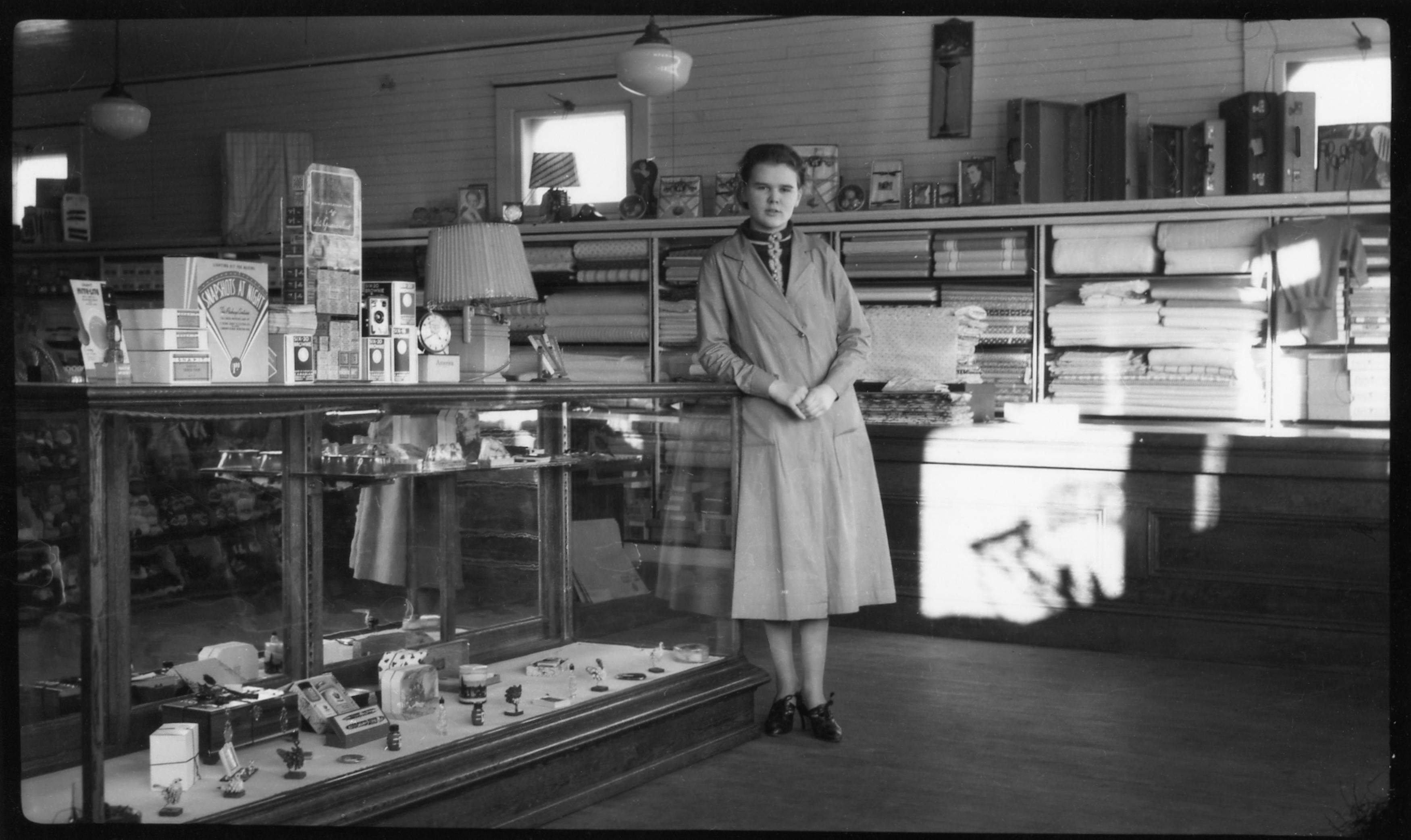 Old black and white photo of Thelma Pepper in a nice coat at 21 years old in a general store.