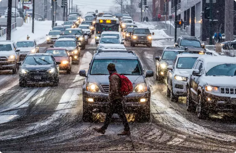 A man walks across a mud-and-snow-covered intersection in Denver, Colorado. Four backed-up lanes of traffic are waiting.