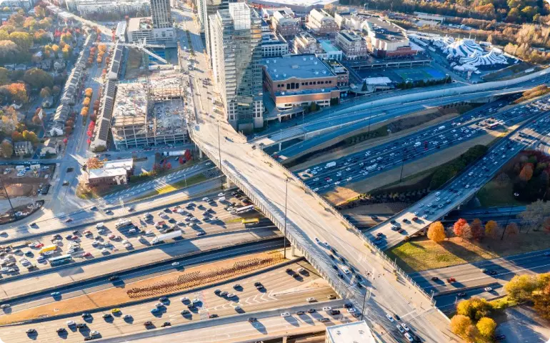 Aerial view of a major highway intersection in Atlanta, Georgia. Four multi-land roads cross from left to right, and one multi-lane highway crosses them on a bridge. Some buildings are visible in the top right-hand quadrant and there are trees on the fringes, but most of the area visible is roads.