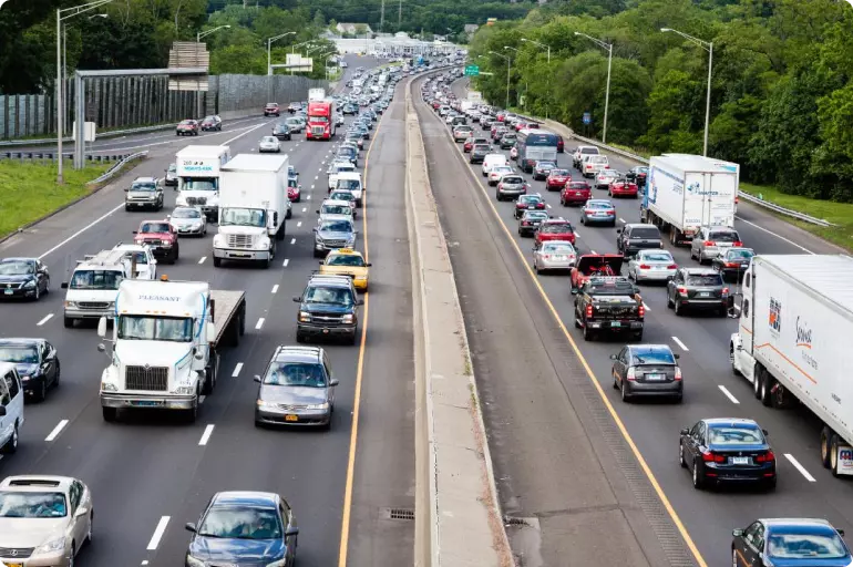Highway through Stamford, Connecticut, clogged with traffic across three lanes in both directions. The highway is lined with grass and green deciduous trees.