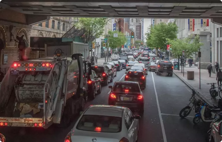 A stream of cars and trucks passes under a bridge in Philadelphia, Pennsylvania. All have their red brake lights on.