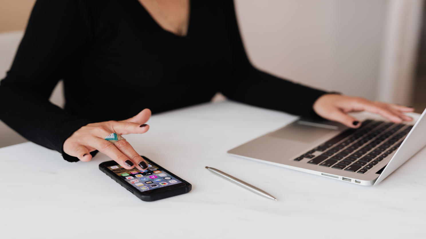 Woman working on the computer while also looking at her phone