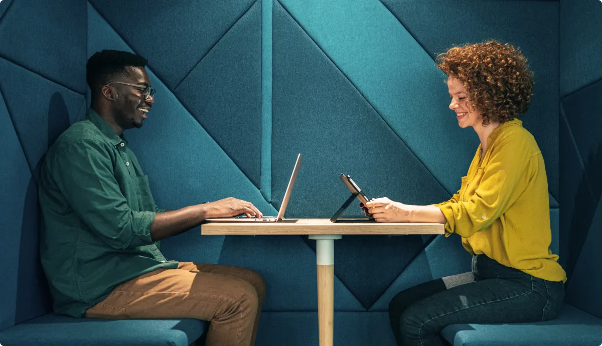 Man and woman sitting across from each other looking at their laptops