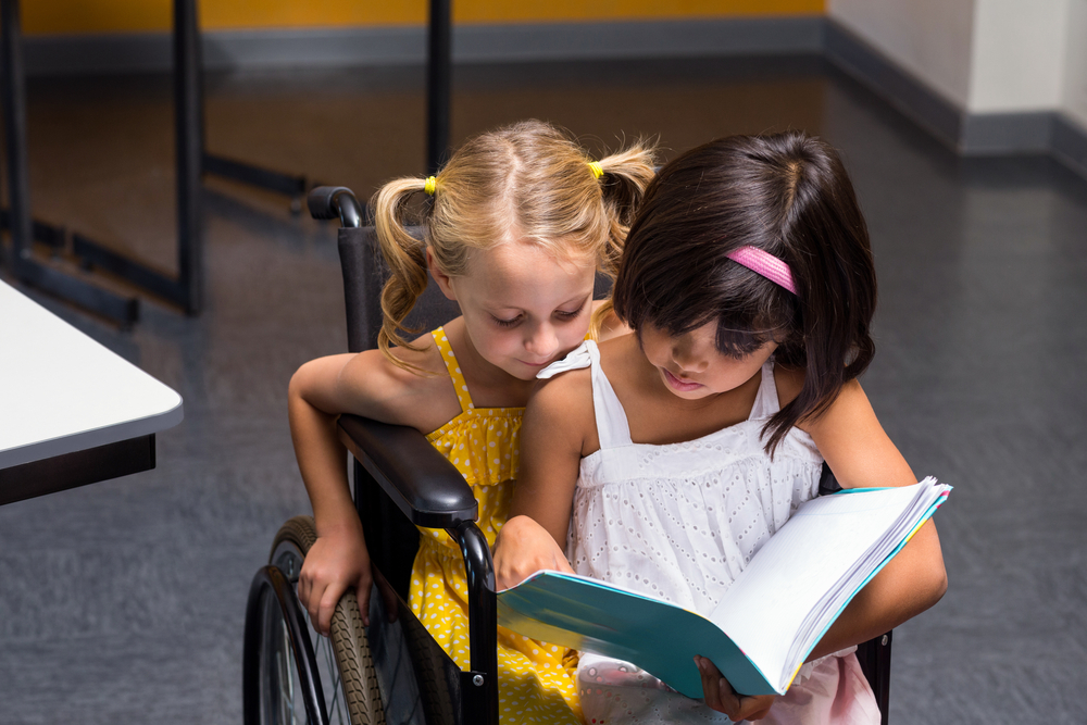 foto di una bambina con disabilità che legge assieme a un'amica