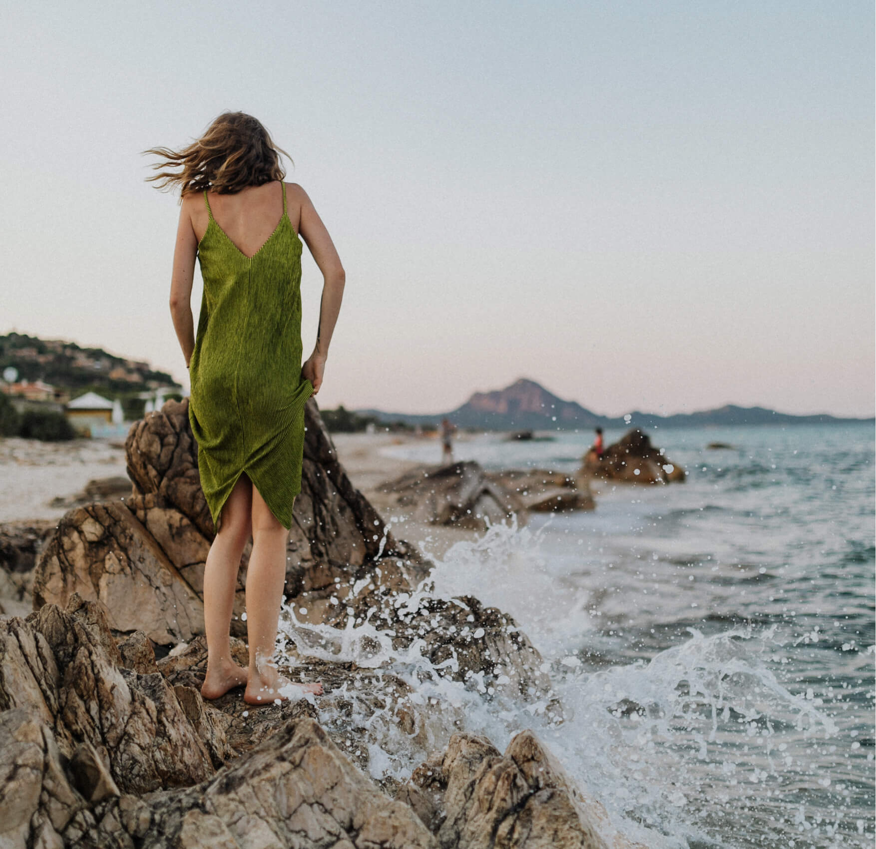 A woman in a green dress on a rock by the sea