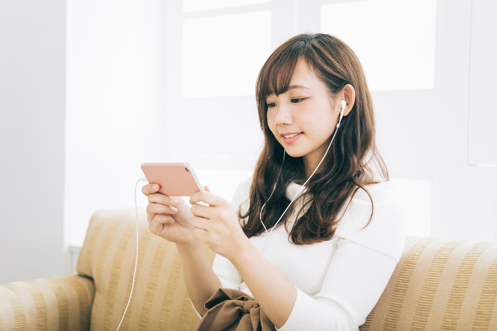 ソファーに座りイヤホンをつけながら横向けにしたスマホを見ている女性