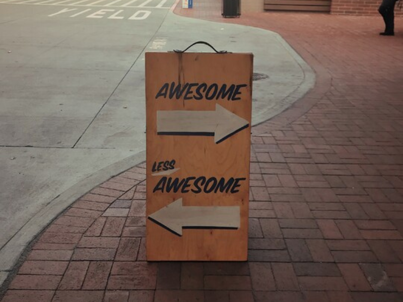 Sandwich board on a street showing arrows pointing in different directions labelled with the words awesome and less awesome