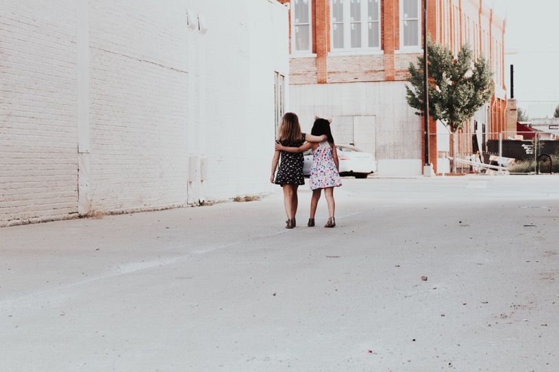 Two little girls walking down a street with linked arms