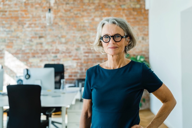 Women wearing glasses, standing in an office with exposed brick wall
