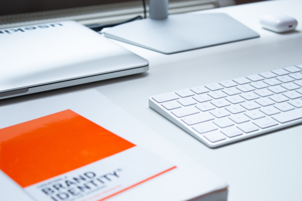 A desk with a laptop, a monitor, keyboard and a book on top