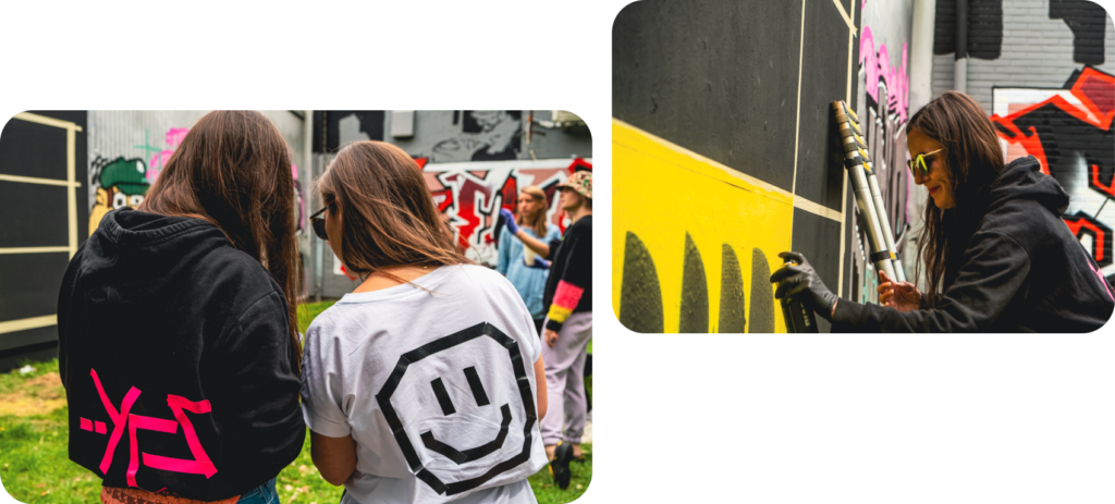 zwei Frauen malen mit Sprühdosen ein geometrisches Muster an die Wand