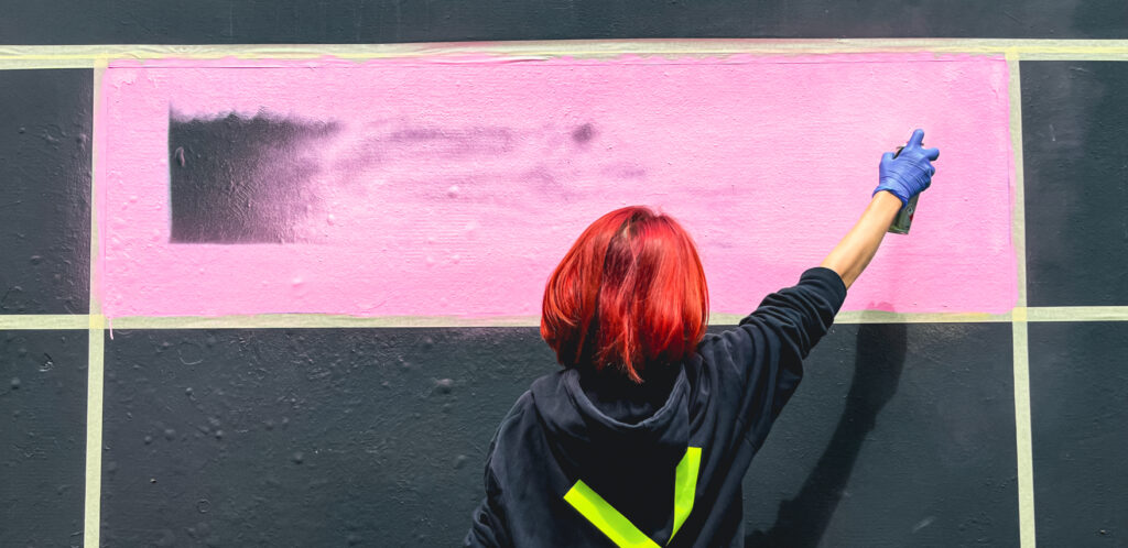 Junge Frau mit roten Haaren malt mit rosa Farbe und Sprühdose an die Wand