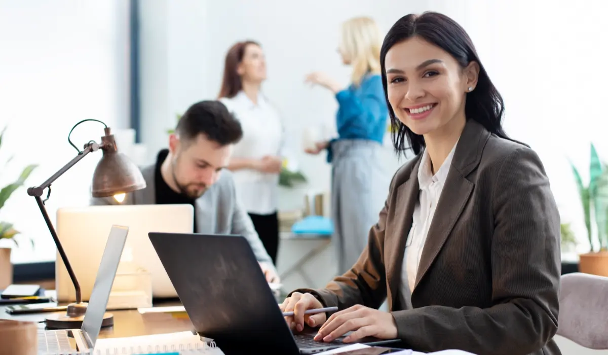 a woman smiling while working on the laptop and 3 people are in the background