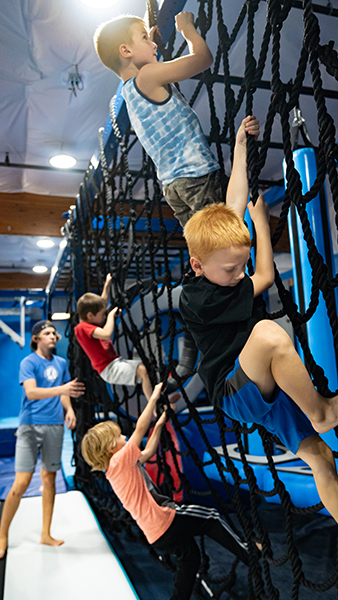 3 young boys climbing a rope wall at Auburn Gymnastics Center