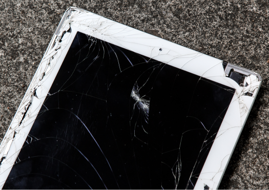A white iPad with a broken screen on concrete