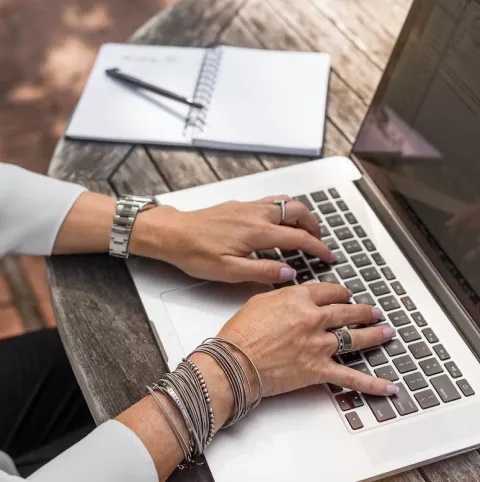 A woman with bracelets typing on the laptop.