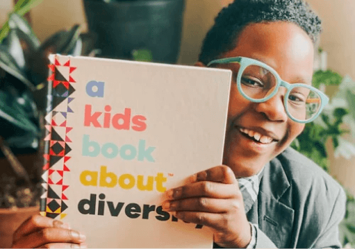 Kid with glasses holding a book about diversity