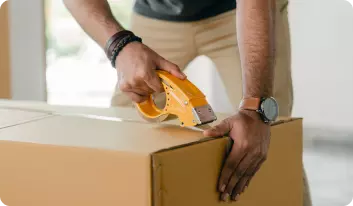 A man sealing a large cardboard box with packing tape.