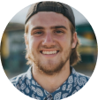 young man smiling wearing a cap backwards and a floral shirt.