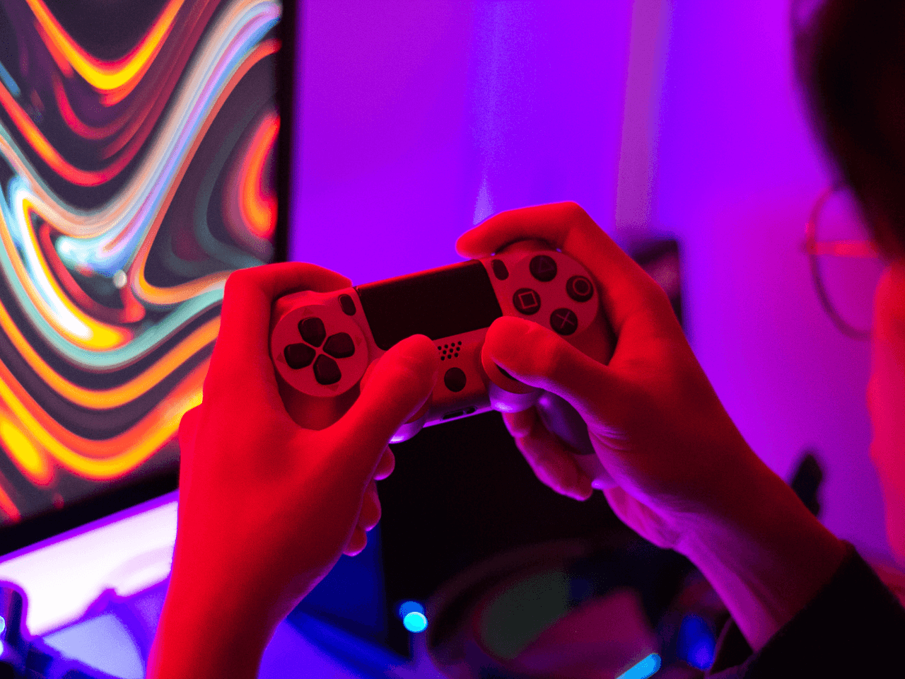 Serenity Eports teams Gamer playing with playstation controller with purple background and colourful monitor 