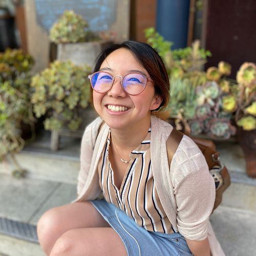 Image of Lulu, a Chinese American girl with glasses and a brown backpack, sitting in front of a row of succulents.