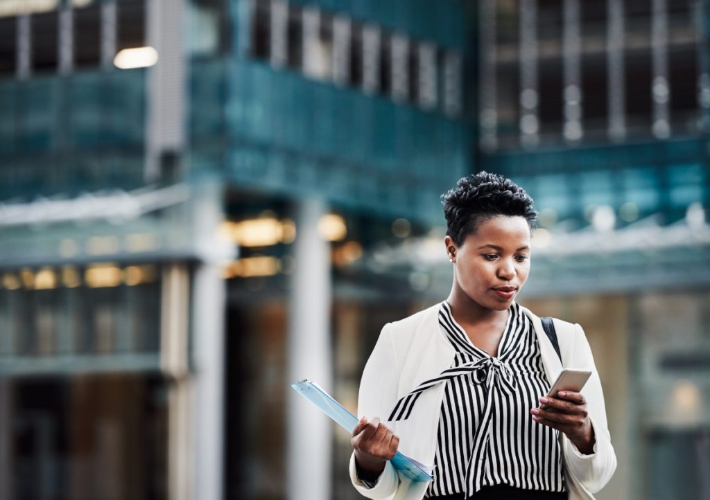 A short-haired woman in professional business attire calls an attorney after leaving her office building in the background.