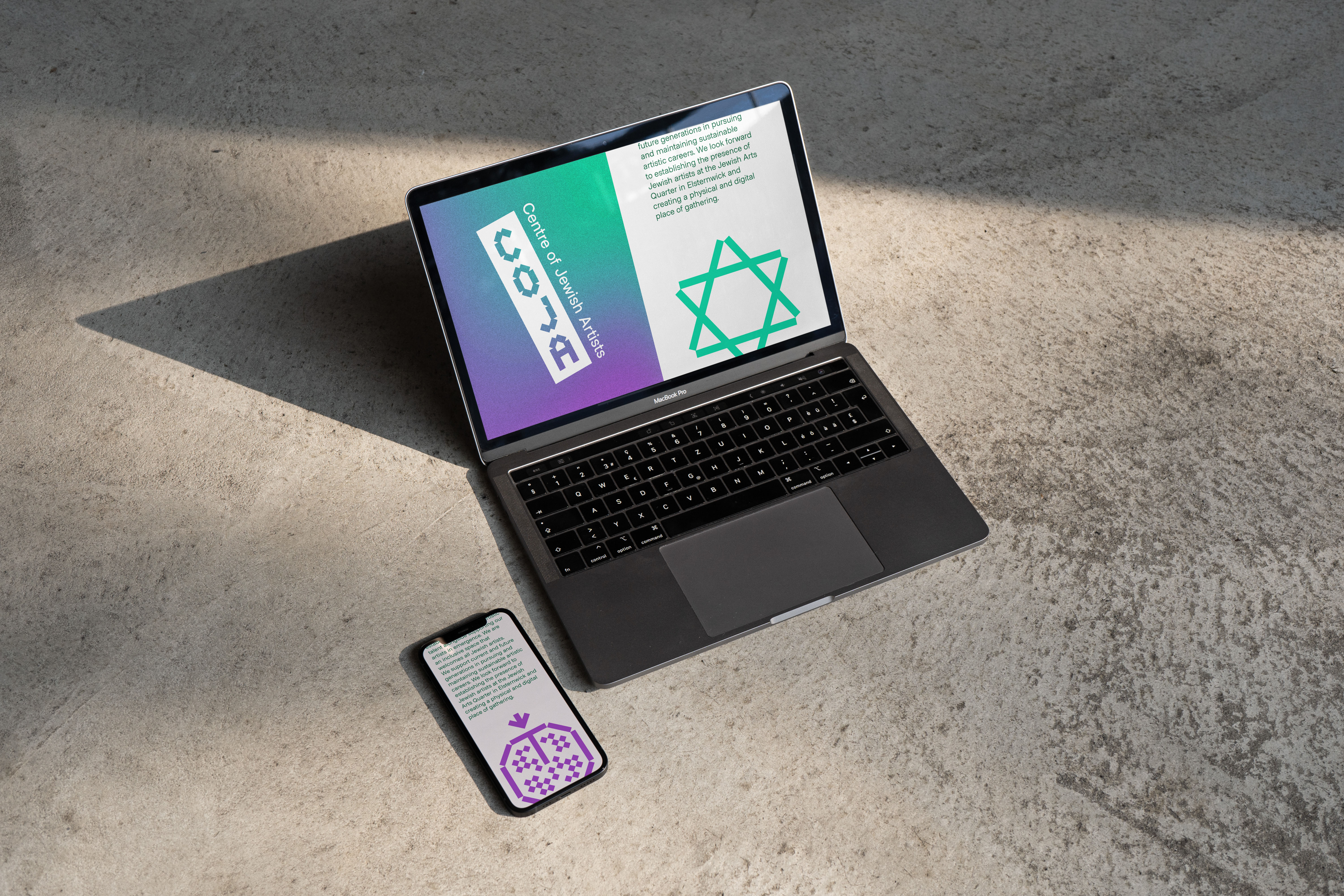 Photo of a laptop and mobile sitting on a concrete background that both have the COJA website on display 