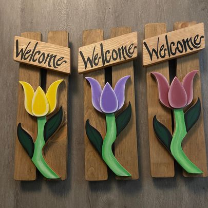 A selection of colored tulips set on pickets with the word "welcome" painted on a sign above them.