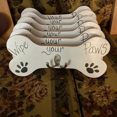 Wooden bones with hangers affixed to them for leashes, or harnesses. The phrase "wipe your paws" is painted on them.
