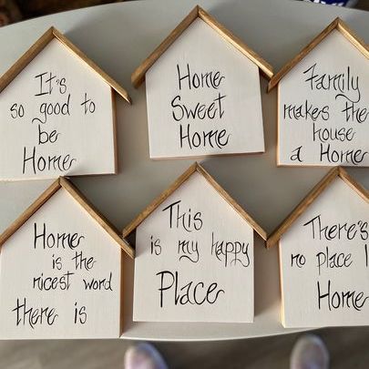 Small wooden houses painted white, with various quotes painted on them. "It's so good to be home," "home sweet home," "This is my happy place," etc.