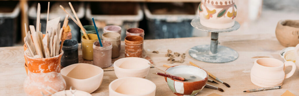 Ceramics And Paints On Wooden Table In Pottery Workshop