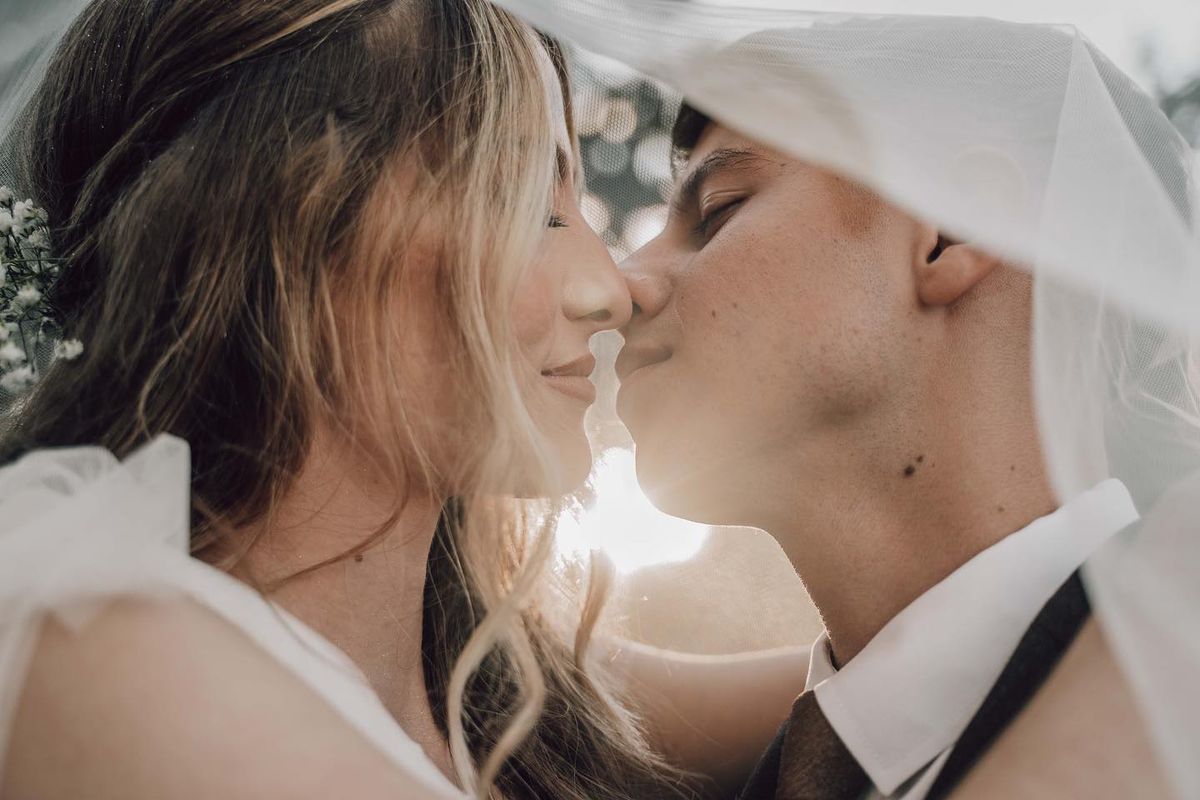 Why We Love Intimate Weddings - Close-up of a bride and groom sharing an intimate moment under the bridal veil, with sunlight softly illuminating their faces