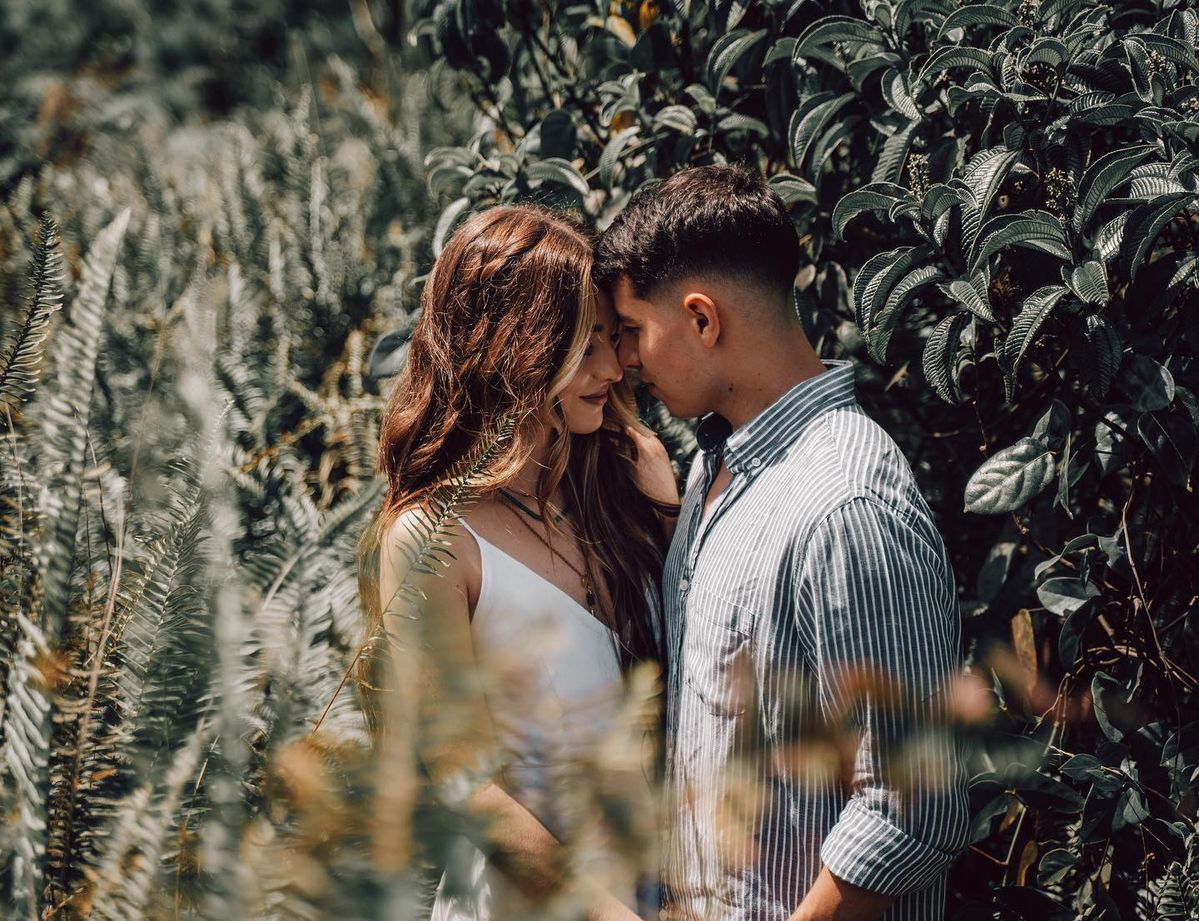 Do I Need a Wedding Planner? - A couple intimately forehead-to-forehead, surrounded by lush green foliage, lost in a moment of love and serenity with a hint of wilderness