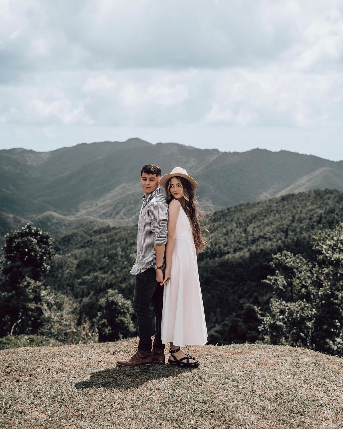 Engagement Photos Yes or No - A couple stands hand in hand on a hilltop, overlooking a breathtaking mountain range, embodying a sense of adventure and romance.