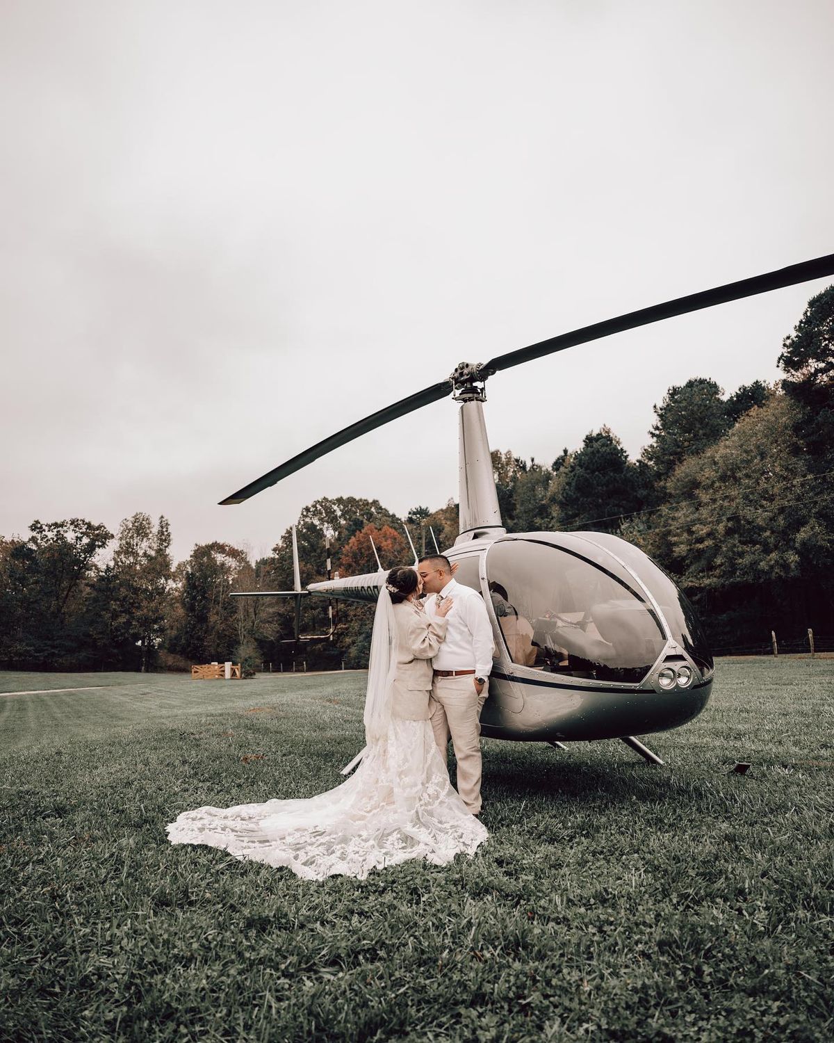Non Traditional Photography - Bride and groom sharing a romantic moment in front of a helicopter on a grassy field, capturing the thrill of their grand wedding exit.