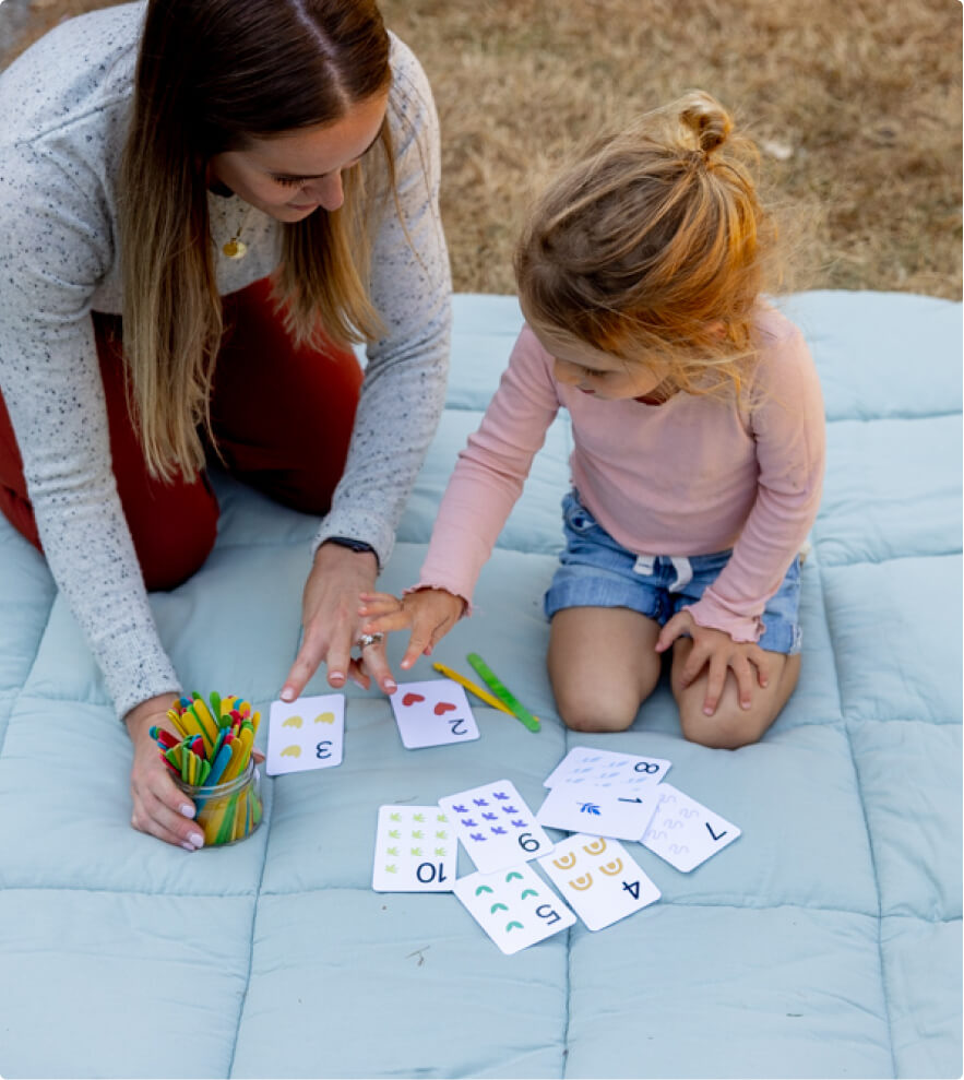A young woman teaching numbers to her daughter with the help of some number cards.