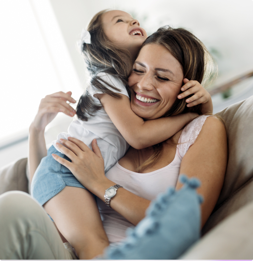 A young woman and her daughter hugging each other and smiling.