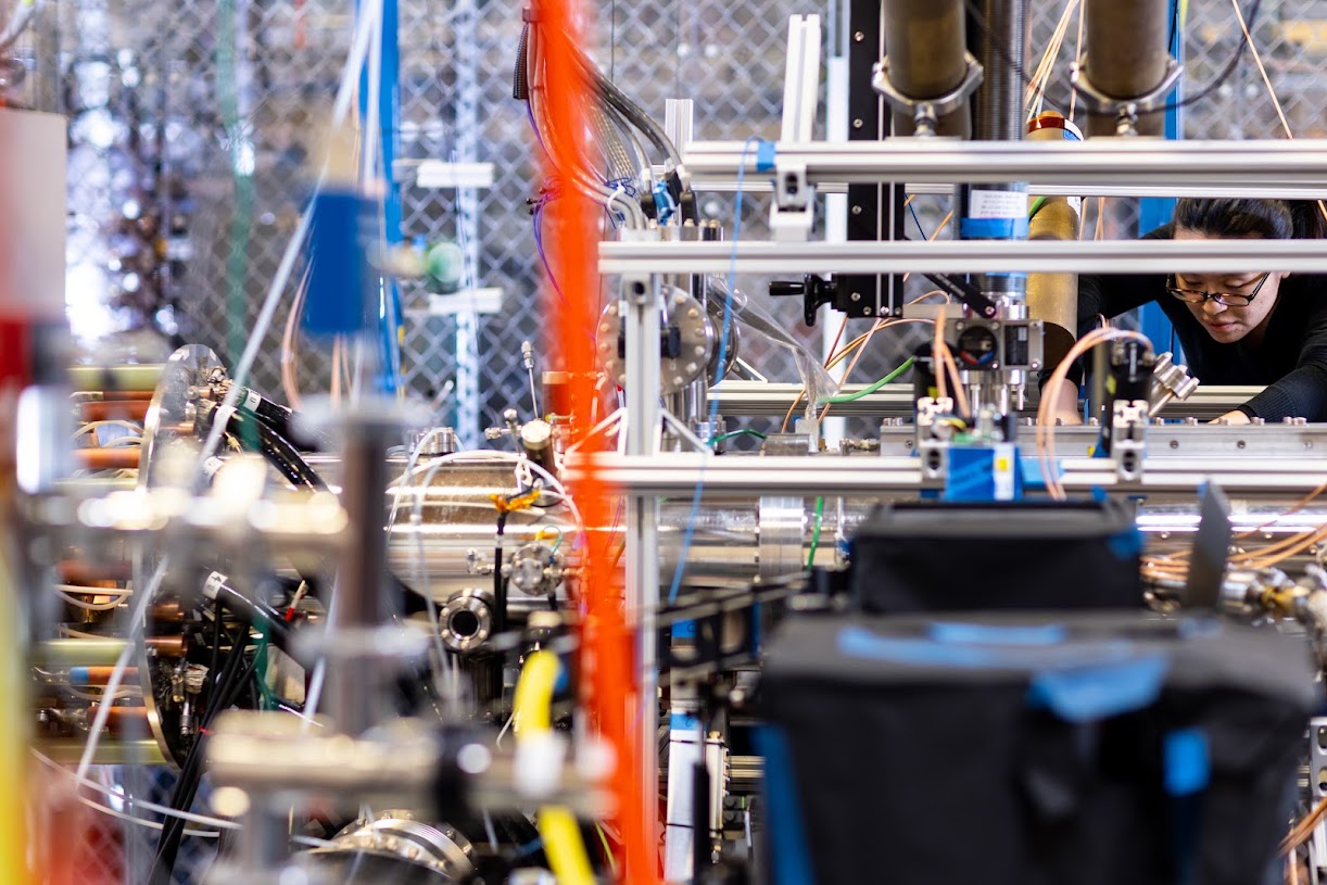 A scientist works on a scintillator detector at the right of a photo showing a silver-colored fusion device, and the wiring and parts around it.