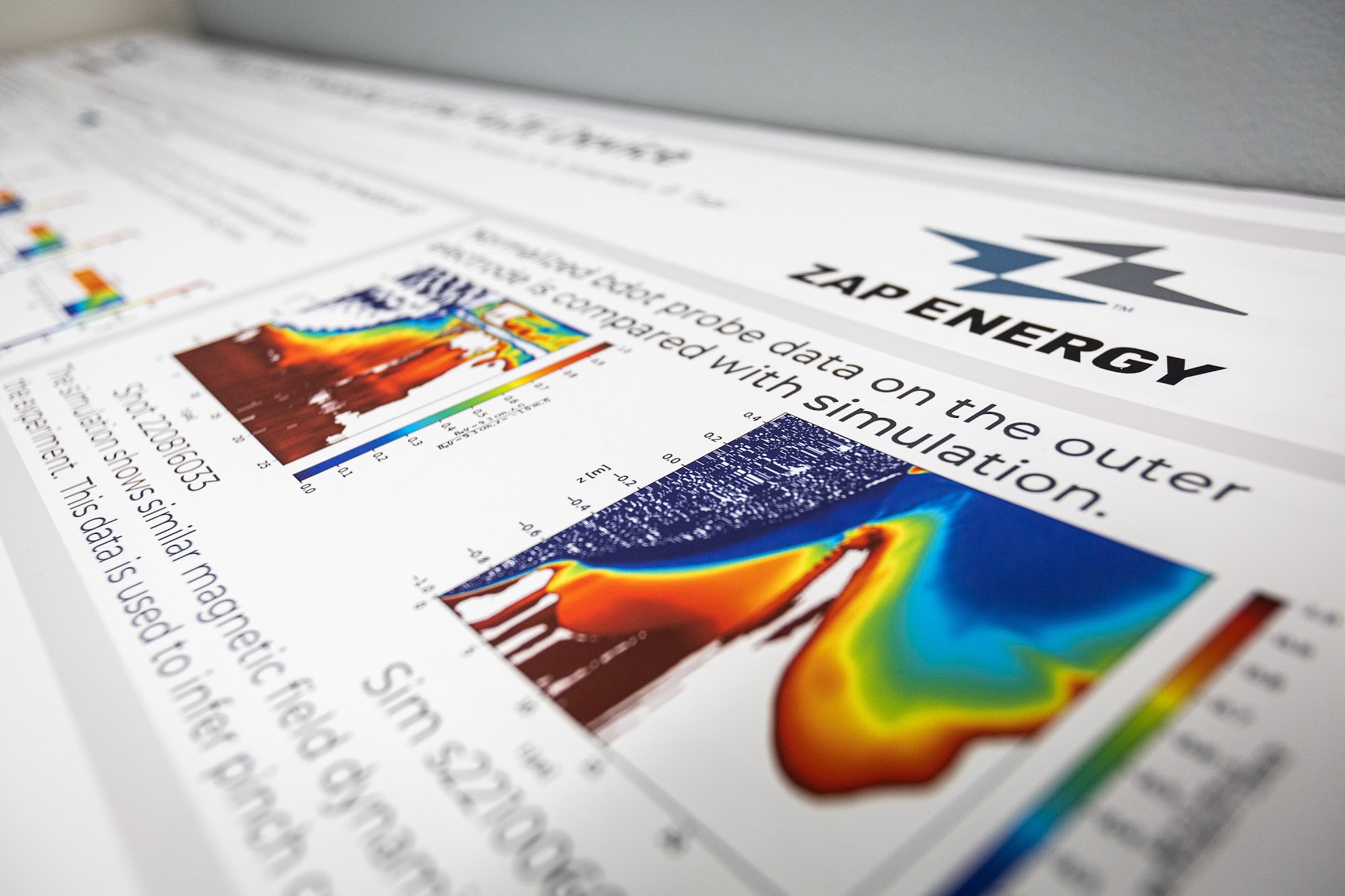 A poster with colorful graphics shows computational models of Zap Energy's sheared-flow-stabilized Z-pinch fusion results.