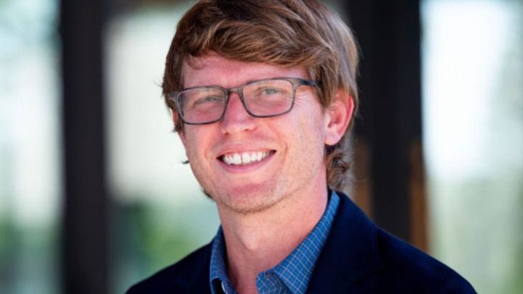Sock Club Senior Operations Coordinator Hamish Roberts pictured smiling in a blazer in an office setting