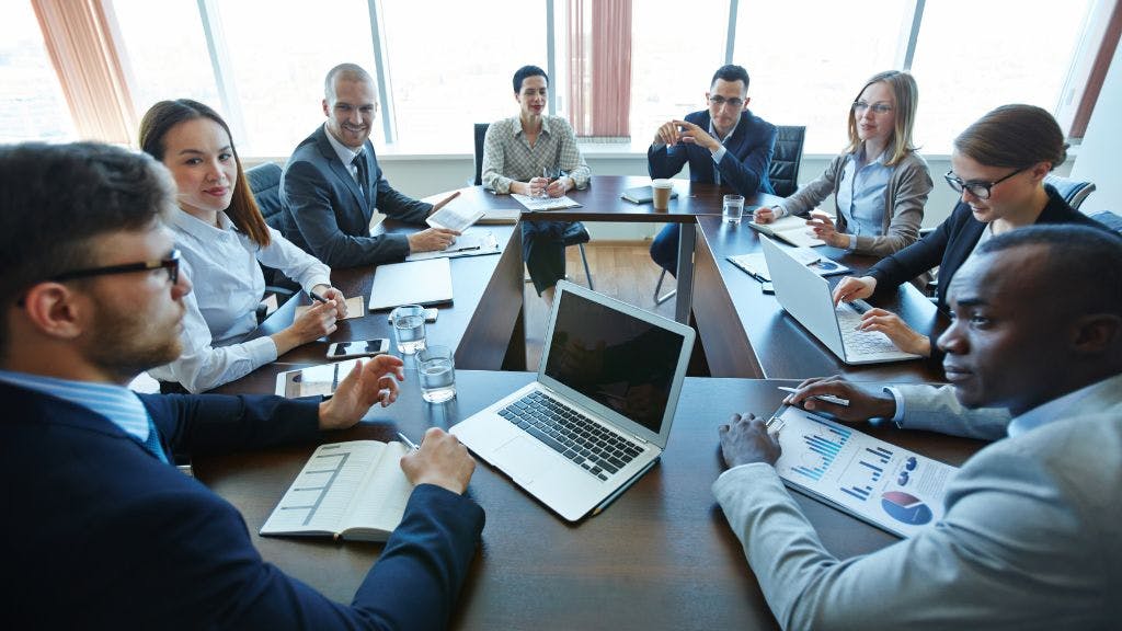 A group of people sitting at desks in a circle at a corporate conference
