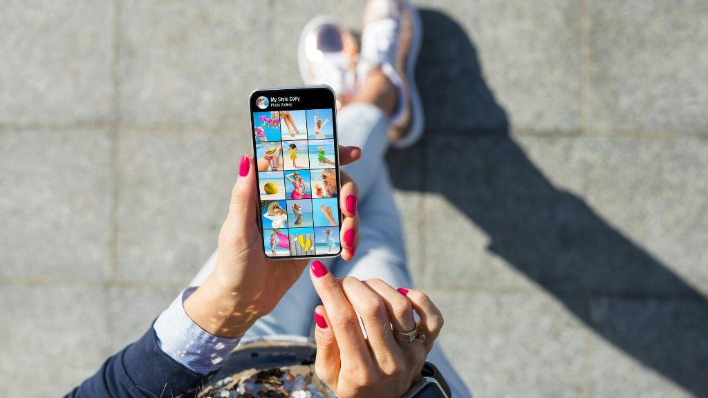 Woman with pink nails shopping for custom merch on social media on her phone outside during the day