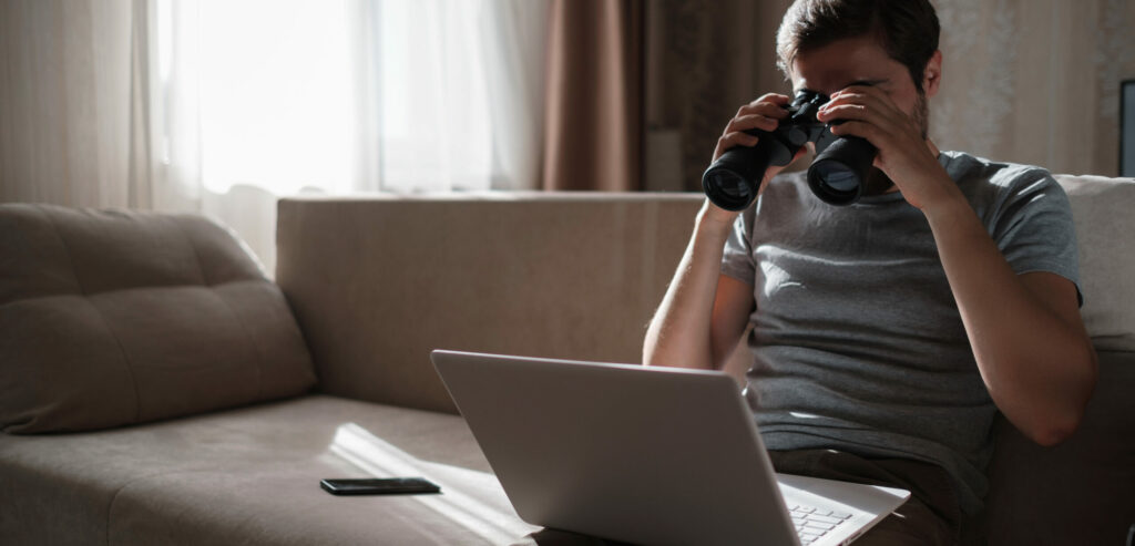Funny Man Looking Searching Binoculars A Laptop On The Table Working At Home Office.