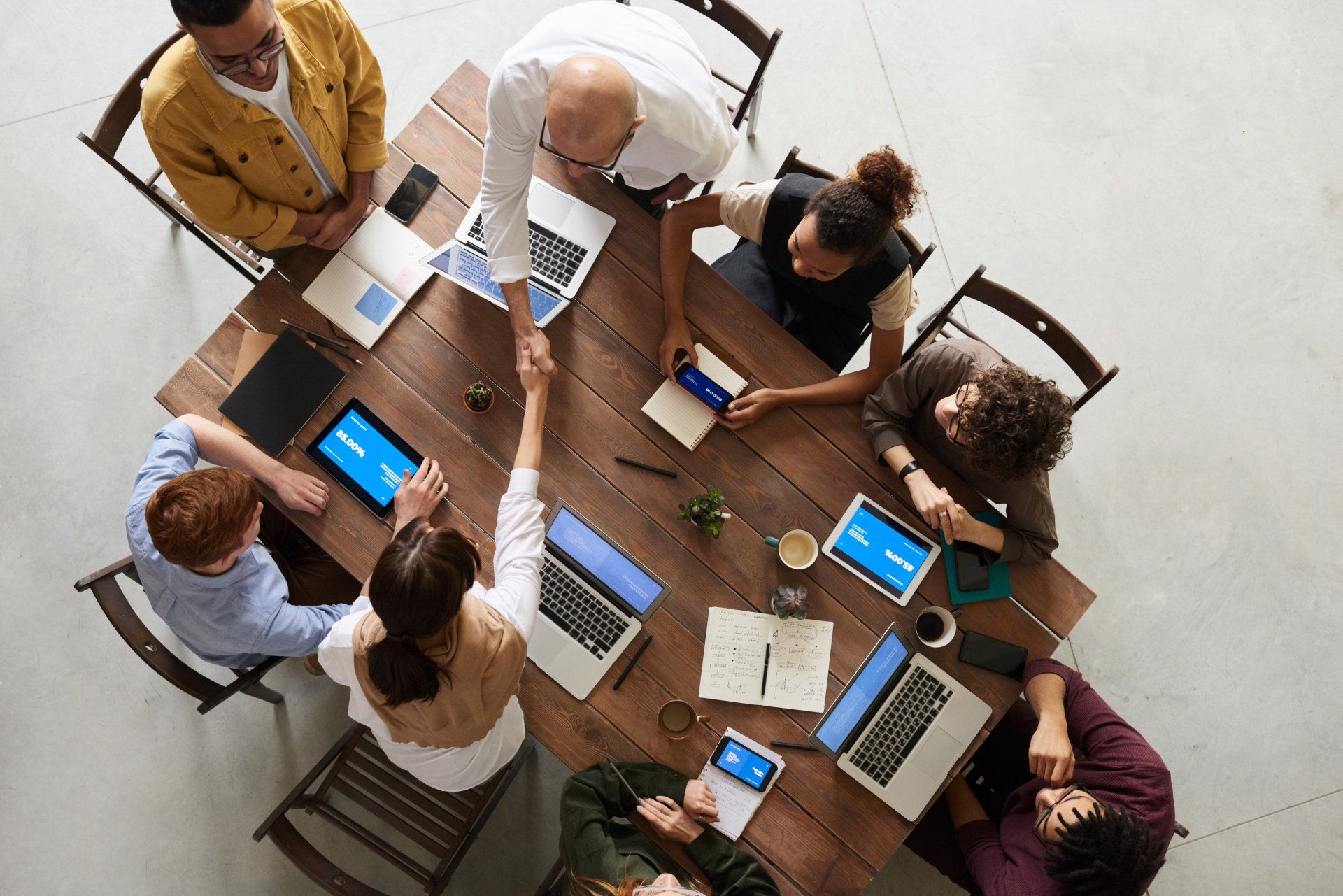 Sales team collaborating at wooden table with laptops and tablets during strategy meeting, representing fractional sales leadership and team development.