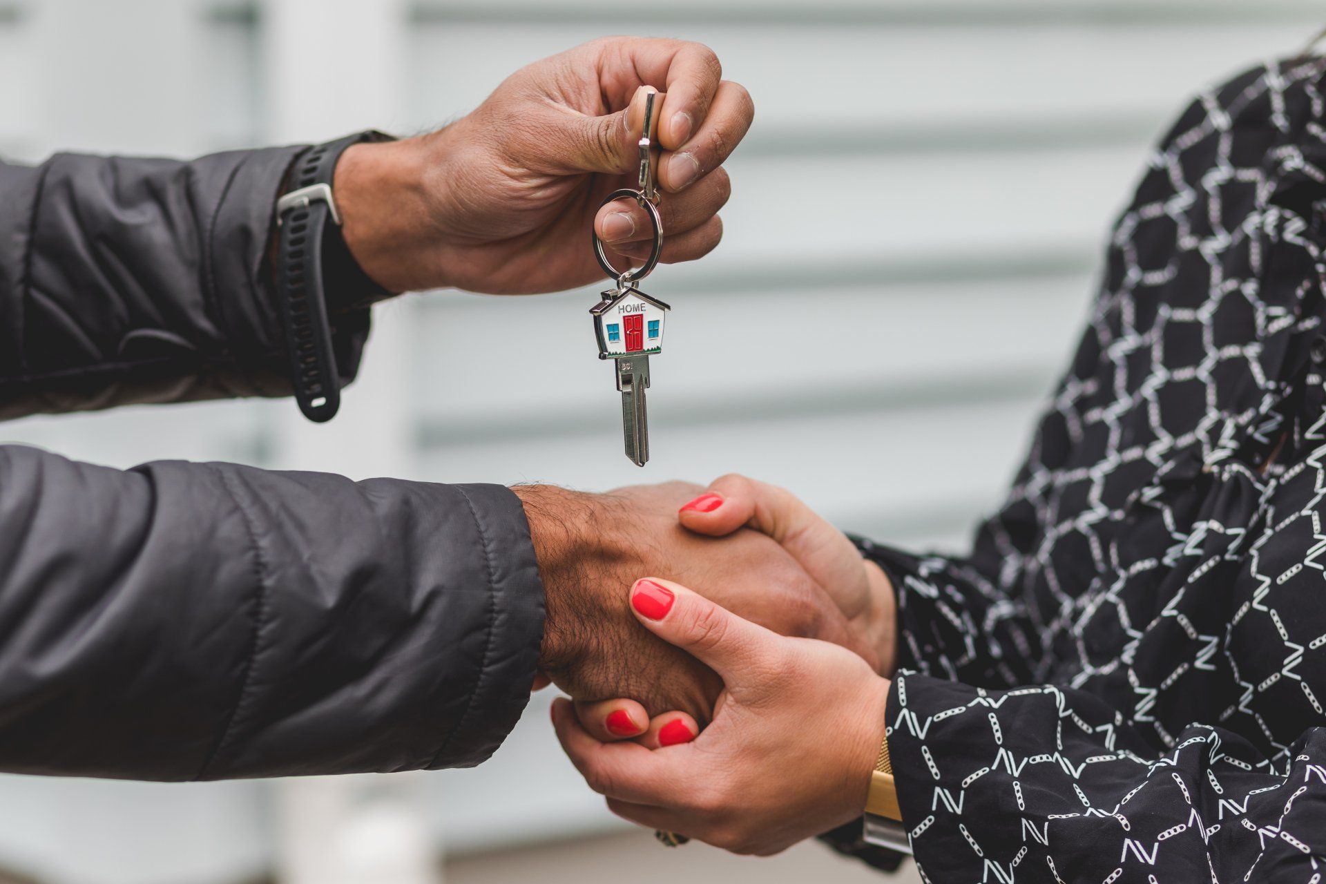 Close-up of two people shaking hands while receiving house keys, symbolizing a successful real estate transaction or home purchase.