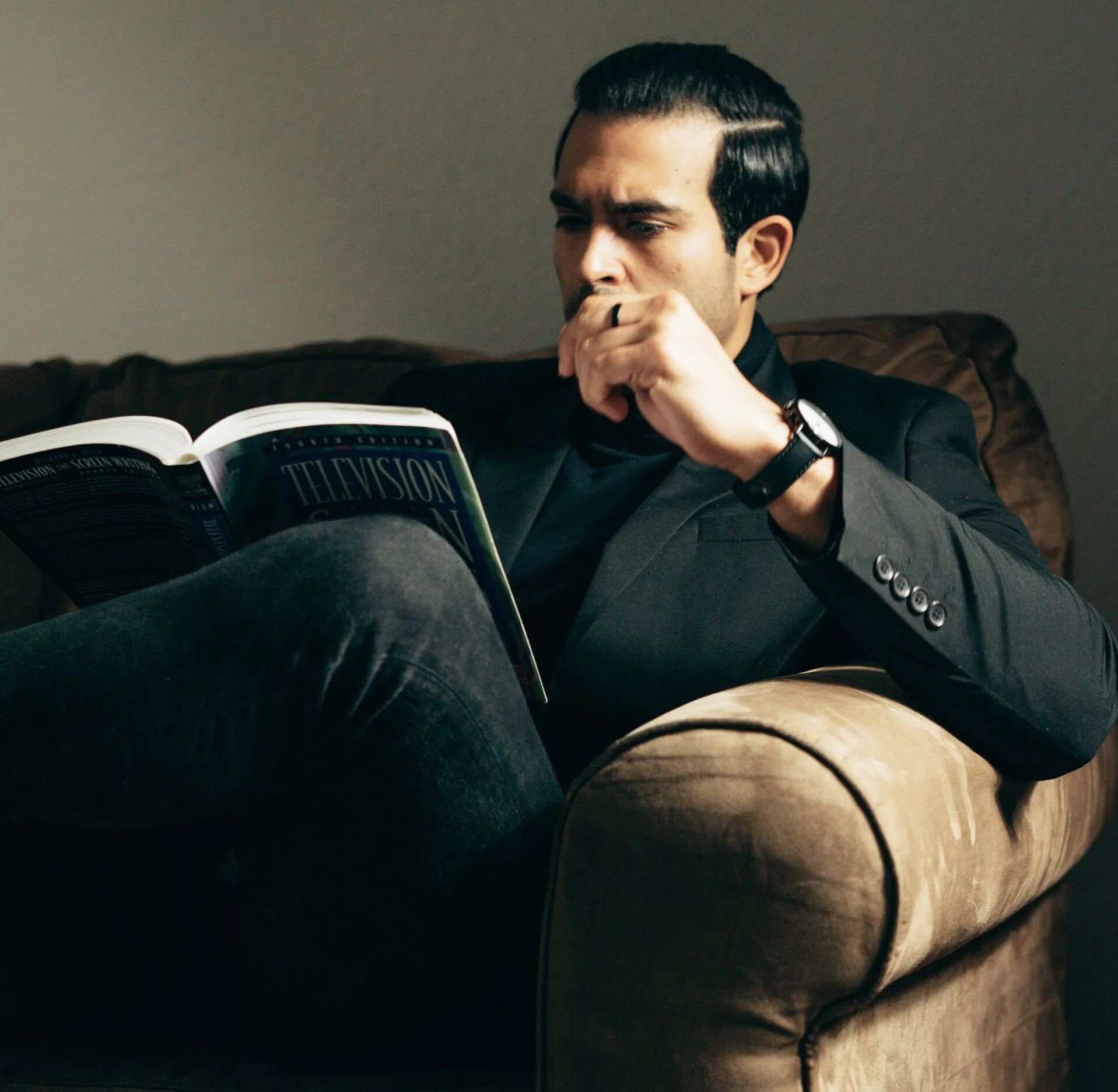 Business professional reading a book on television production while sitting on a couch, focused on learning and strategy.