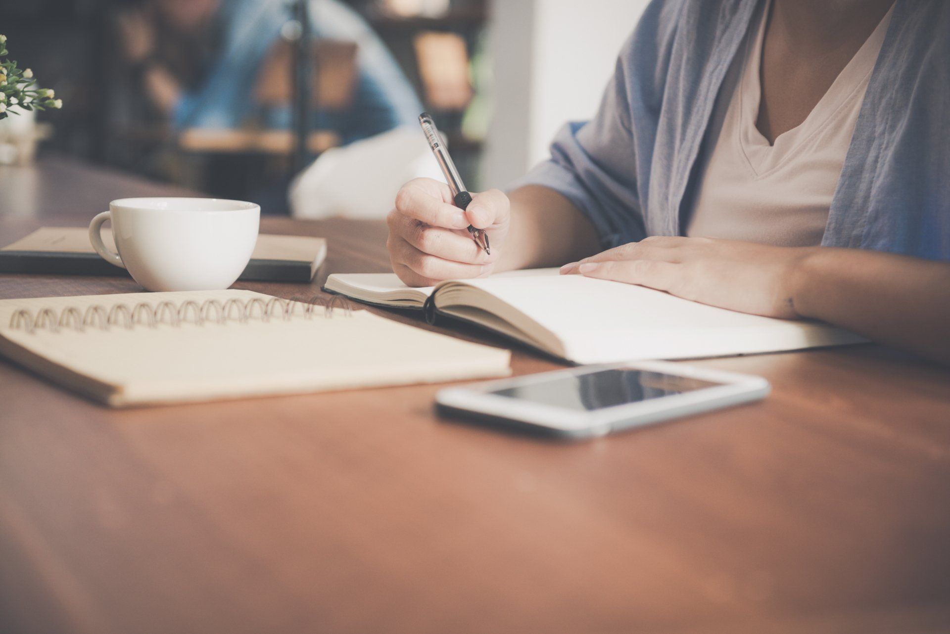 Business leader taking notes in notebook at desk with coffee, smartphone, and planner, focusing on strategy and personal development.