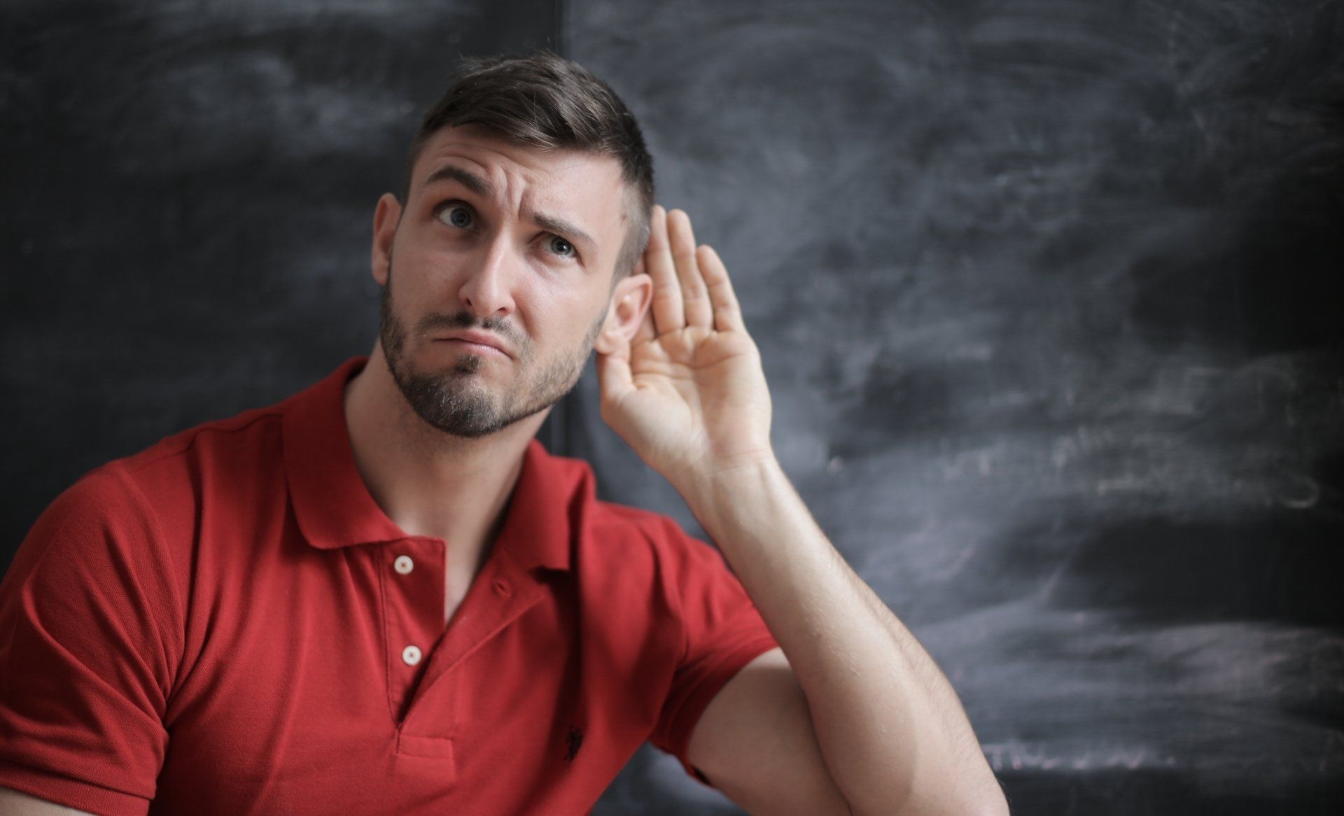 Curious business professional practicing active listening, a key leadership trait, while standing in front of a chalkboard background.