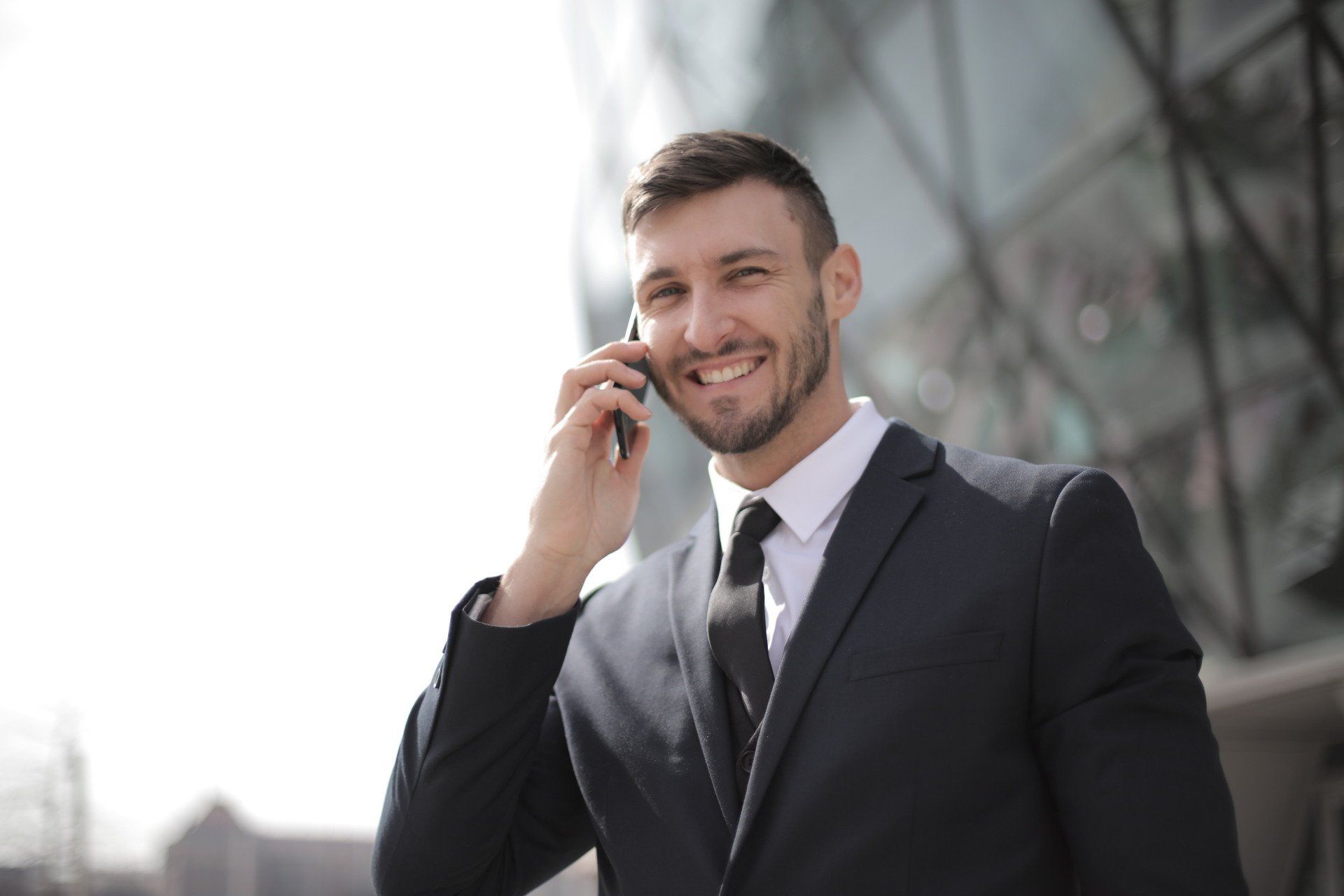 Confident sales leader in business suit smiling while talking on phone outside office building, representing fractional revenue leadership.